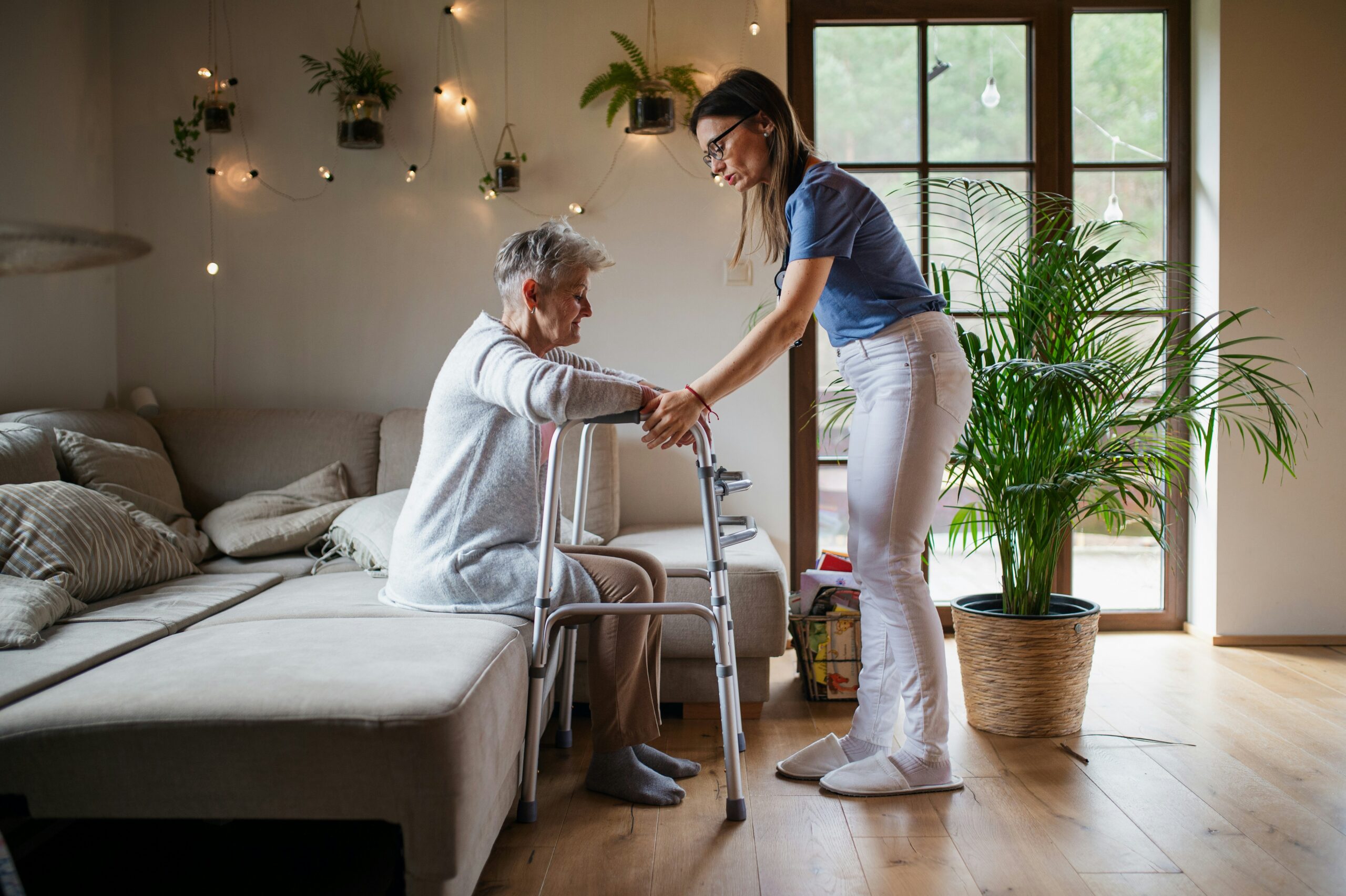 A woman assists an elderly woman using a walker, providing support and guidance in a caring manner.